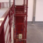 Piros rácsos teheremelő a galériaszinten, korlát mellett